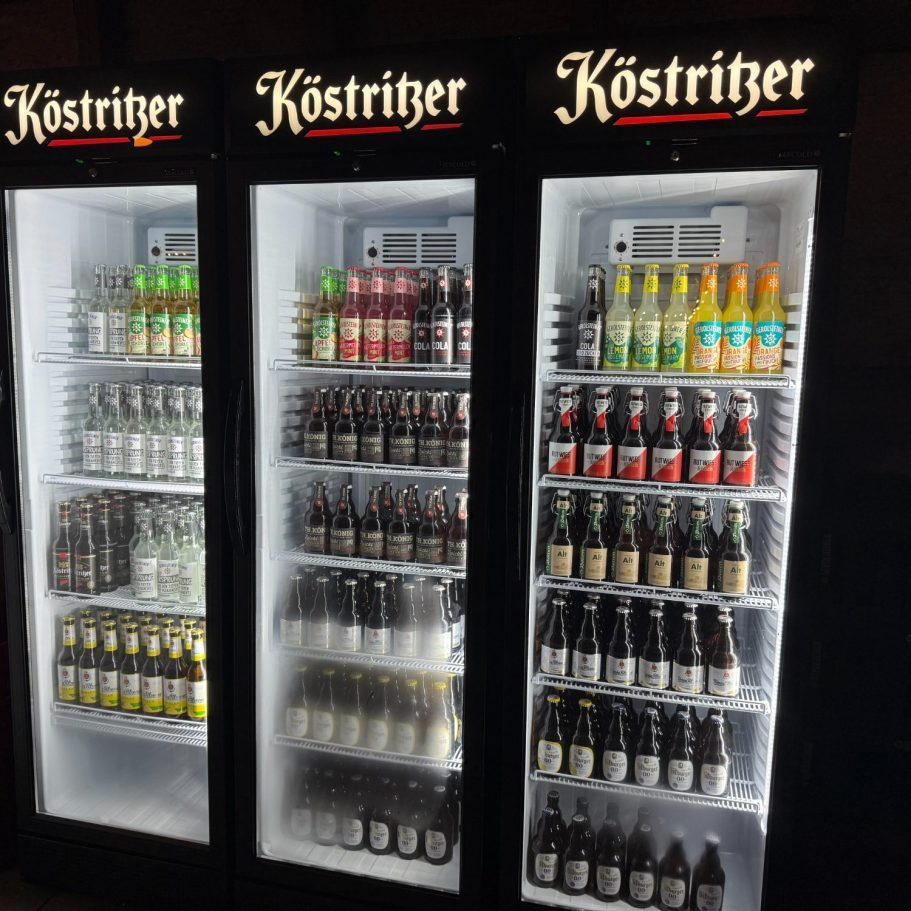 Drei gefüllte beleuchtete Getränkekühlschränke, mit diversen Getränken bestückt. Darunter Bier, Wasser, Limonade